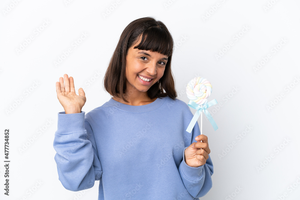 Young mixed race woman holding a lollipop isolated on white background saluting with hand with happy expression Young mixed race woman holding a lollipop isolated on white background saluting with hand with happy expression