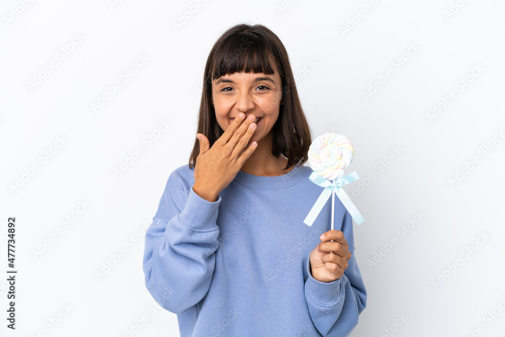 Young mixed race woman holding a lollipop isolated on white background happy and smiling covering mouth with hand Young mixed race woman holding a lollipop isolated on white background happy and smiling covering mouth with hand