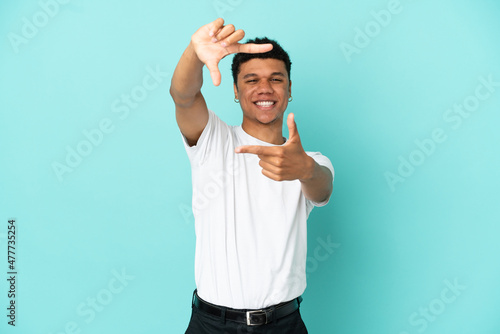 Young African American man isolated on blue background focusing face. Framing symbol