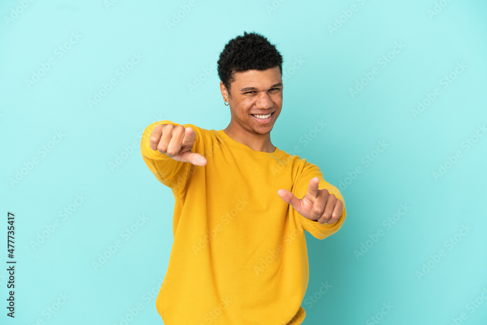 Young African American man isolated on blue background pointing front with happy expression Young African American man isolated on blue background pointing front with happy expression