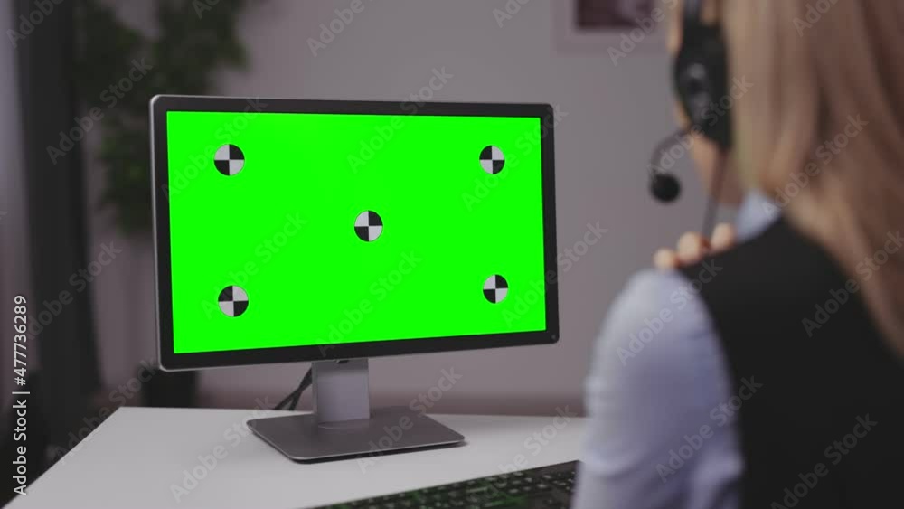 Back view of mature lady in headset talking and gesturing during video call on pc. Business woman having online meeting while staying at home. Focus on chroma key monitor. Back view of mature lady in headset talking and gesturing during video call on pc. Business woman having online meeting while staying at home. Focus on chroma key monitor.