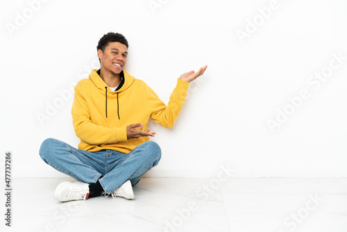 Young African American man sitting on the floor isolated on white background extending hands to the side for inviting to come