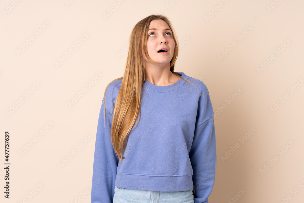 Obraz premium Teenager Ukrainian girl isolated on beige background looking up and with surprised expression