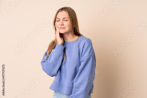 Teenager Ukrainian girl isolated on beige background with toothache © luismolinero
