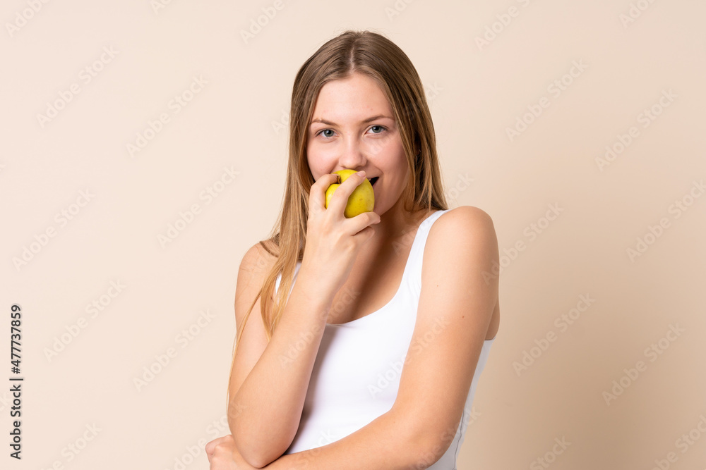 Teenager Ukrainian girl isolated on beige background eating an apple Teenager Ukrainian girl isolated on beige background eating an apple