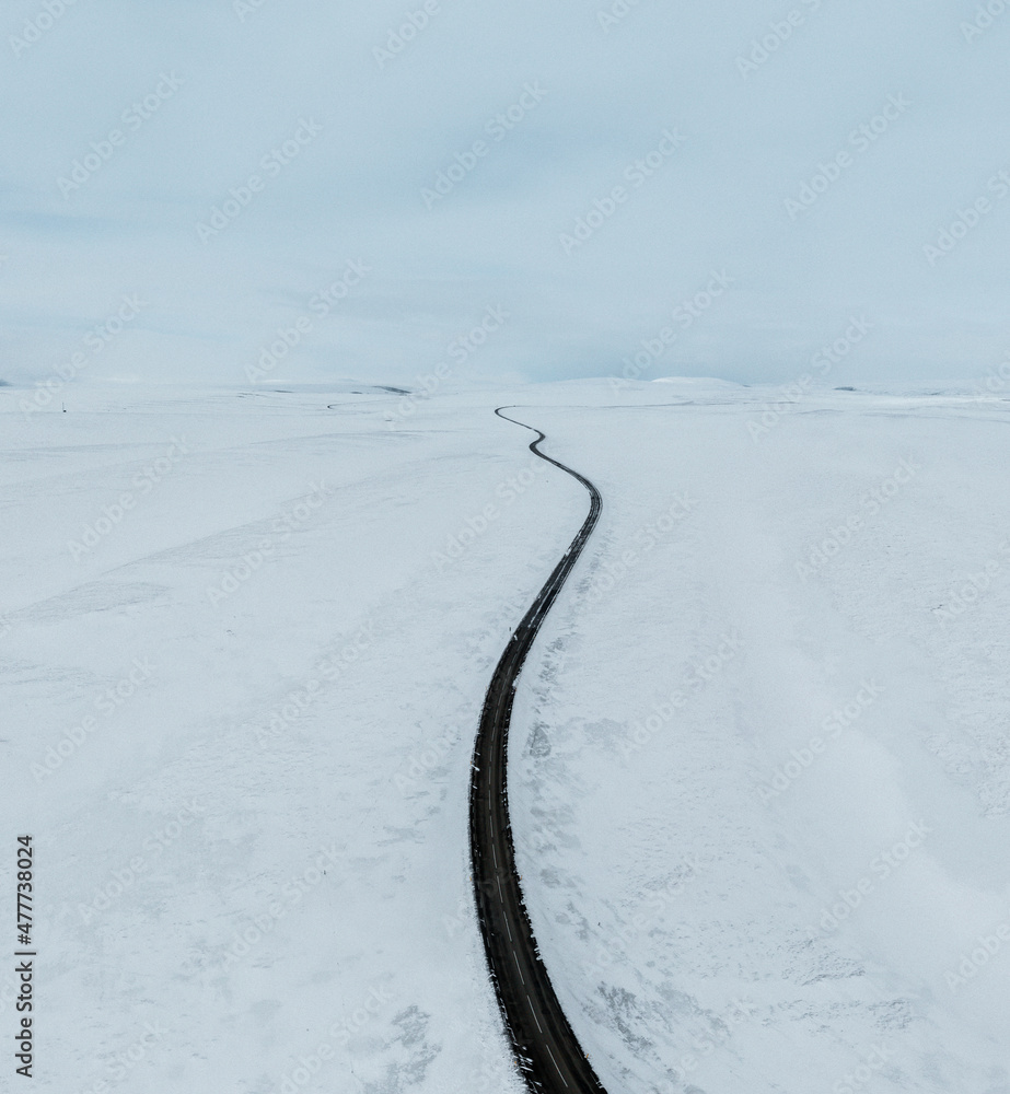 aerial drone view Uphill road landscape in winter at Iceland. Asphalt road with sideways full of snow during winter with blue sky.
