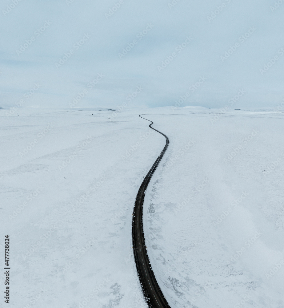 Obraz premium aerial drone view Uphill road landscape in winter at Iceland. Asphalt road with sideways full of snow during winter with blue sky.