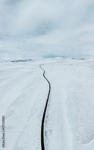 aerial drone view Uphill road landscape in winter at Iceland. Asphalt road with sideways full of snow during winter with blue sky. © Mathias
