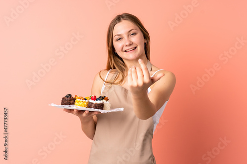 Pastry Ukrainian chef holding a muffins isolated on pink background inviting to come