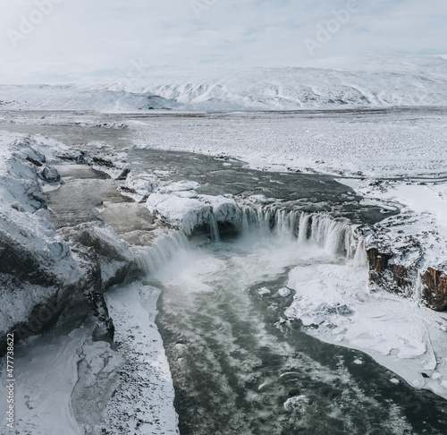 Drone shot of Godafoss waterfall, Iceland, taken from a high angle. Aerial view of the powerful cascade, river and snow covered rocks. Late autumn, early winter scene.