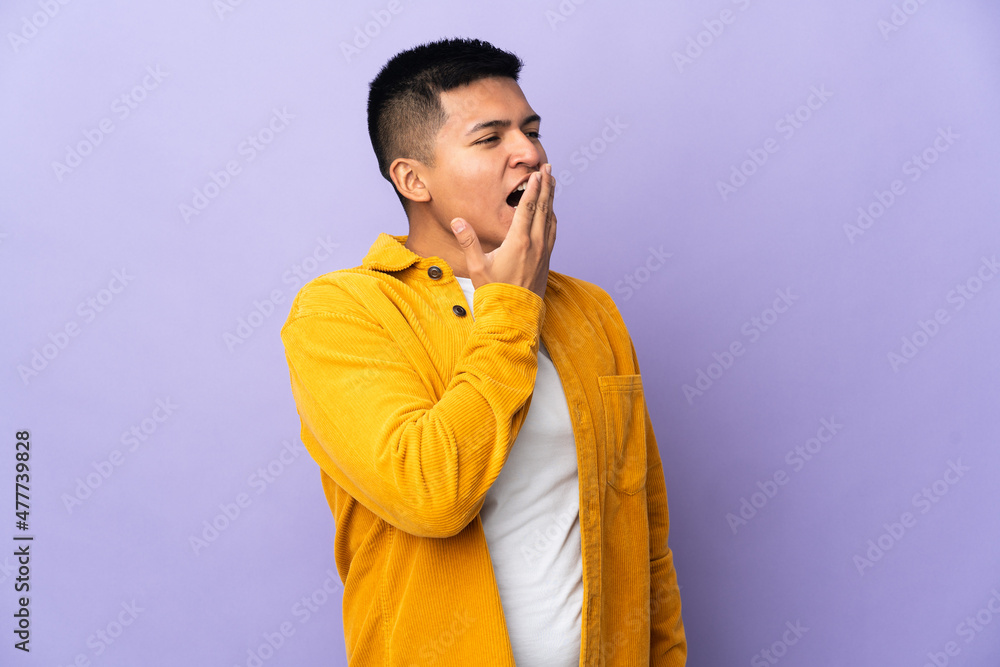 Fototapeta premium Young Ecuadorian man isolated on purple background yawning and covering wide open mouth with hand