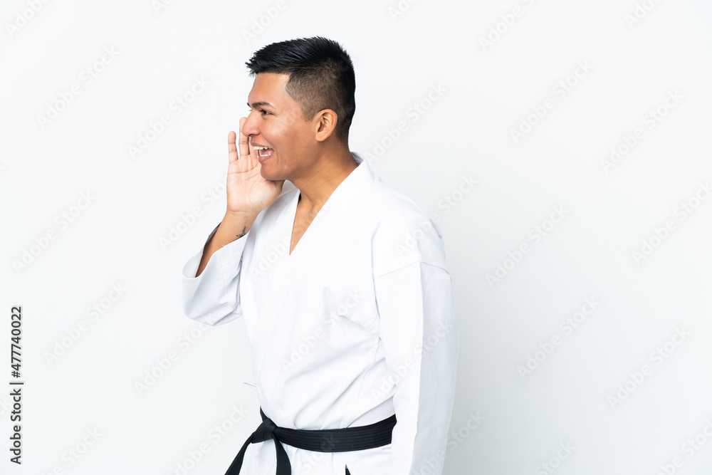 Young Ecuadorian man doing karate isolated on white background shouting with mouth wide open to the side Young Ecuadorian man doing karate isolated on white background shouting with mouth wide open to the side
