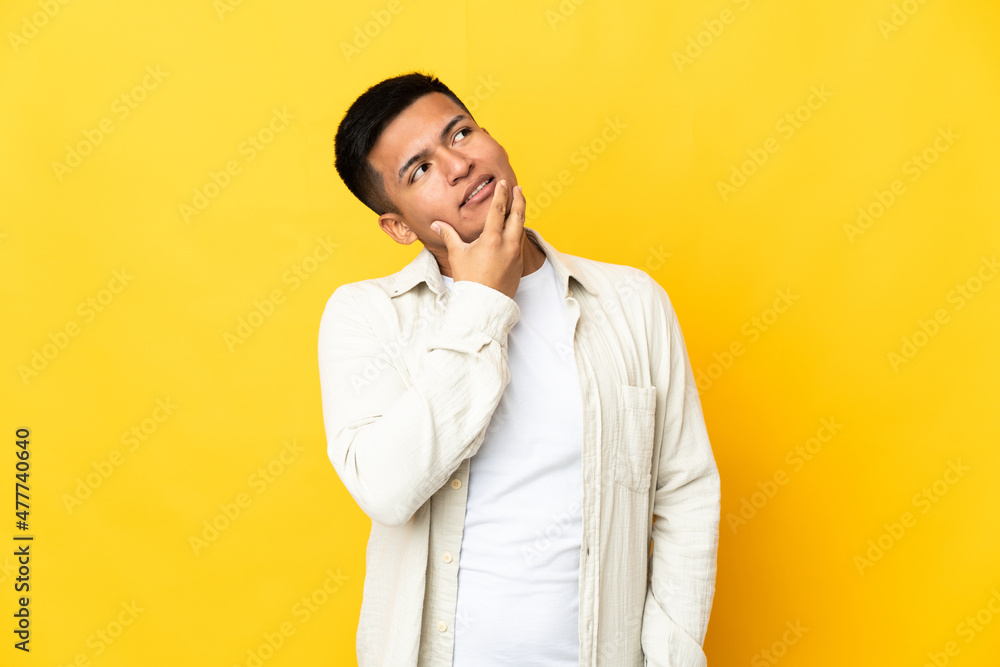 Obraz premium Young Ecuadorian man isolated on yellow background looking up while smiling