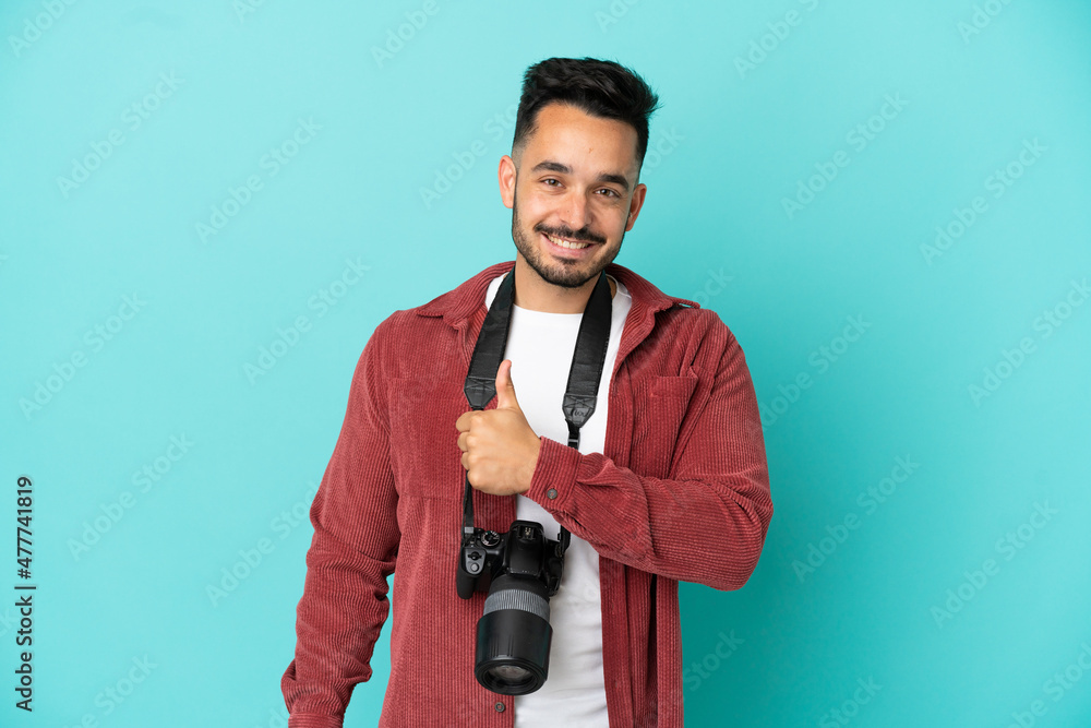 Naklejka premium Young photographer caucasian man isolated on blue background giving a thumbs up gesture