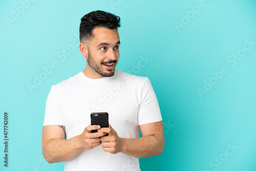 Young caucasian man isolated on blue background using mobile phone and looking up © luismolinero