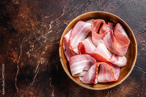 Smoked sliced bacon in wooden plate. Dark background. Top view. Copy space