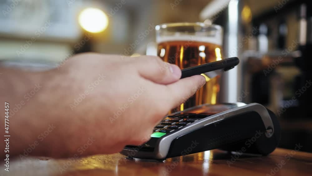 Buying beer and paying by smartphone closeup. Bearded barman standing