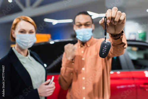 selective focus of key in hand of blurred african american man in medical mask showing success gesture near car dealer. © LIGHTFIELD STUDIOS