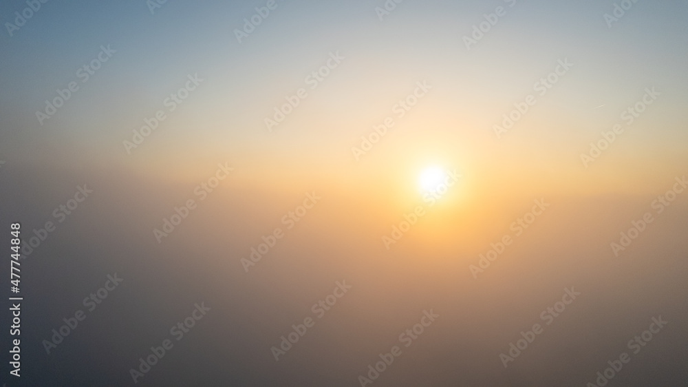 Aerial View. Flying in fog, fly in mist over the early morning clouds in the rising sun. Aerial camera shot. Flight above the clouds towards the sun with the mist clouds floating by. Misty weather