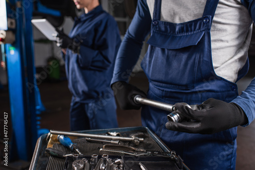 Cropped view of mechanic holding wrench near blurred colleague with digital tablet in garage.