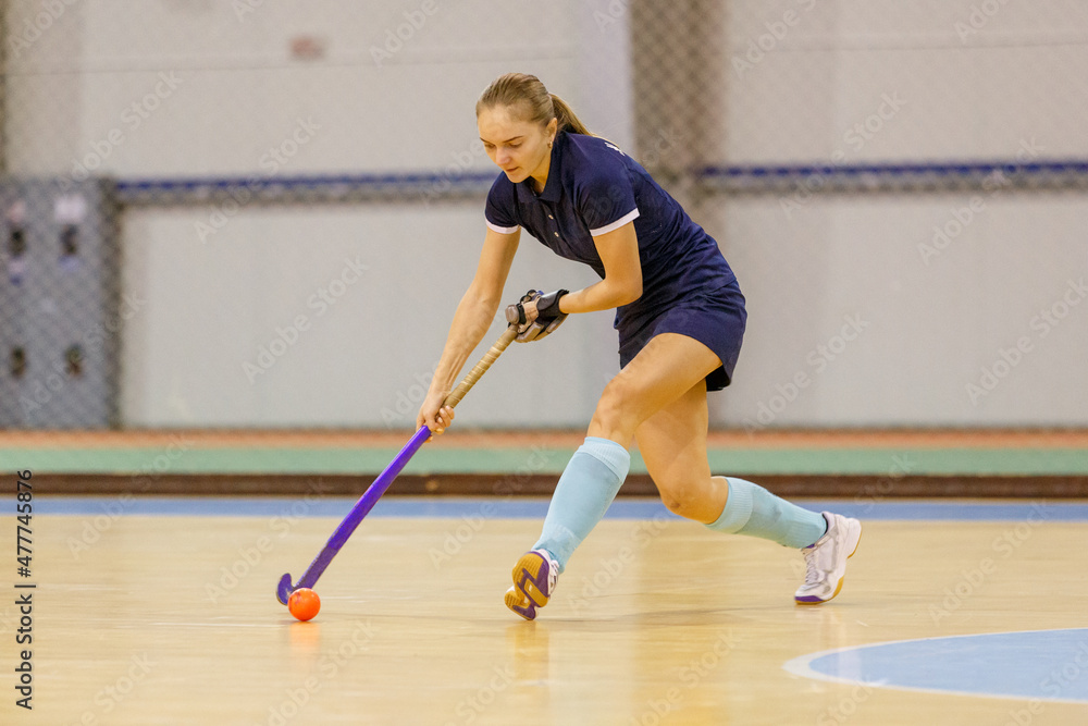 Young woman playing indoor hockey and leading the ball in attack.