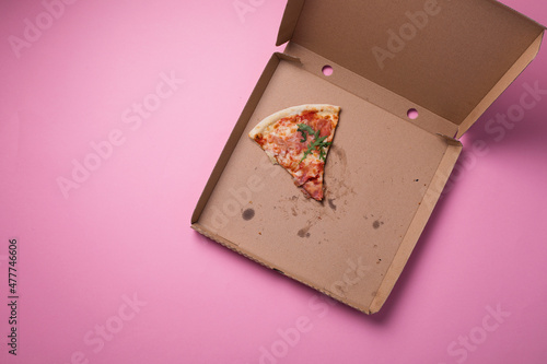 Last slice of pizza, food leftovers on empty pizza cardboard box pink background, top view photo