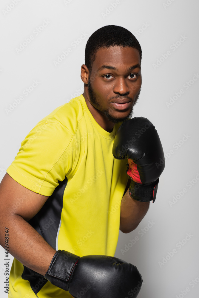 strong african american sportsman working out in boxing gloves isolated on grey.