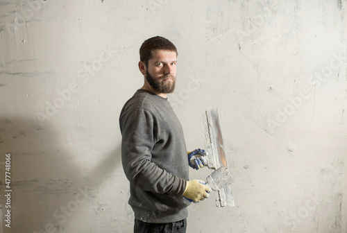 a plasterer man with a beard stands at a rough plastered wall with spatulas