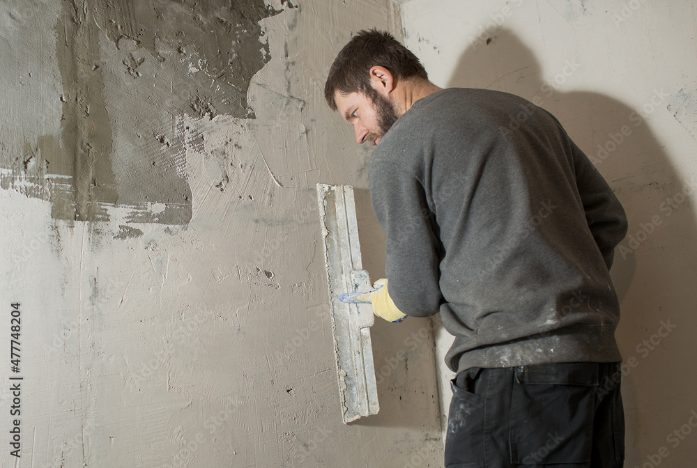 a plasterer man with a beard stands at a rough plastered wall with spatulas.
a plasterer man with a beard stands at a rough plastered wall with spatulas.