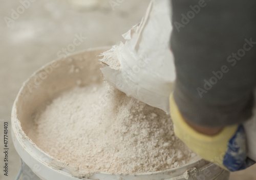 the process of pouring a dry putty plaster solution from a bag in a bucket close-up.