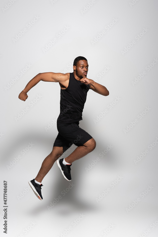 full length of fast african american sportsman levitating while running on grey. full length of fast african american sportsman levitating while running on grey.