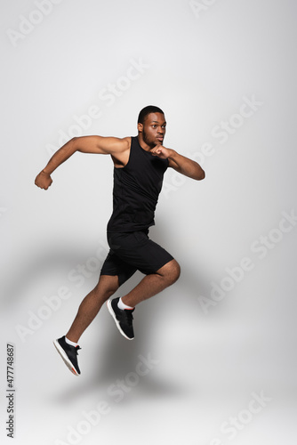 full length of fast african american sportsman levitating while running on grey.
