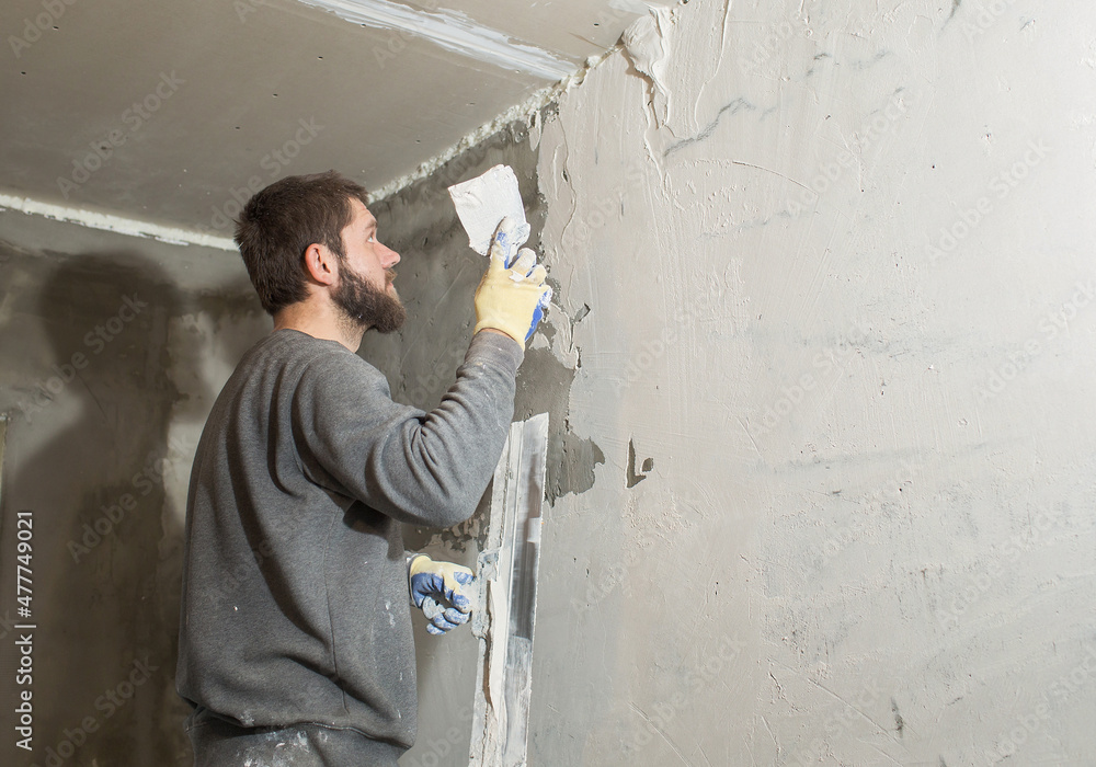 a male plasterer with a beard plasters a concrete wall with a spatula..