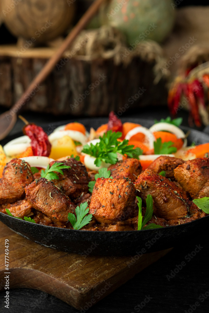 Stew with meat and vegetables in black iron dish. Traditional gourmet goulash in a rustic kitchen Stew with meat and vegetables in black iron dish. Traditional gourmet goulash in a rustic kitchen