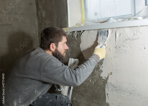 a man with a beard plasterer plasters a concrete wall under the windowsill with a spatula. © Olga