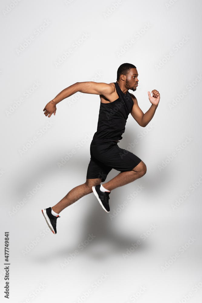full length of african american sportsman levitating while running on grey.