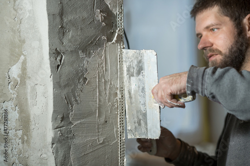 a man with a plasterer beard mounts a perforated painting corner on the corner of the doorway of the room, in his hand a spatula.