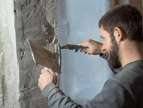 a man with a plasterer beard mounts a perforated painting corner on the corner of the doorway of the room, in his hand a spatula.