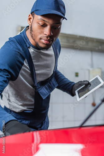 african american technician in uniform holding digital tablet with blank screen near blurred car.
