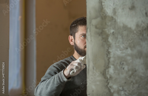 a man with a beard plasterer plasters with a spatula a concrete corner of a doorway with a perforated corner , a close-up portrait
