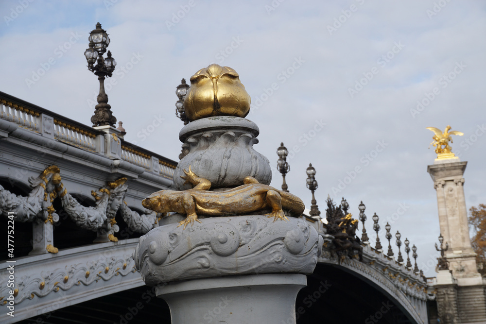 Obraz premium closeup on gold salamander on pillar and bridge alexandre 3 with numerous lamp posts in paris france