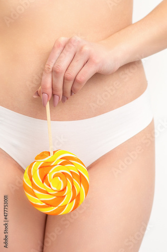 Hand of a woman wearing white panties holding lollipop on a stick covering the intimate area, the concept of intimate depilation, problems of intimate hygiene photo