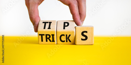 Tips and tricks symbol. Businessman turns wooden cubes and changes the word tricks to tips. Beautiful yellow table, white background. Business, tips and tricks concept. Copy space. photo