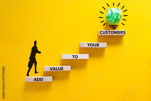 Add value to your customers symbol. Concept words 'Add value to your customers' on wooden blocks on a yellow background, copy space. Businessman icon, light bulb. Business, customers value concept.