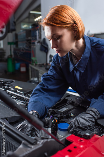 forewoman in uniform fixing motor of car in workshop.