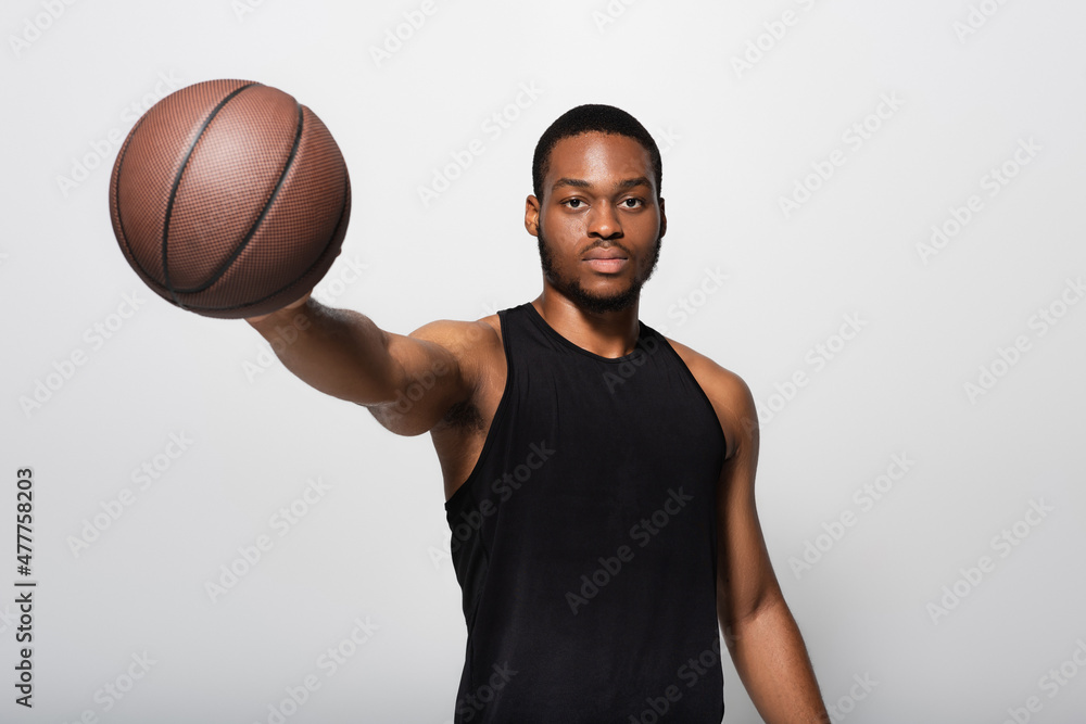 young african american player with outstretched hand holding basketball isolated on grey.