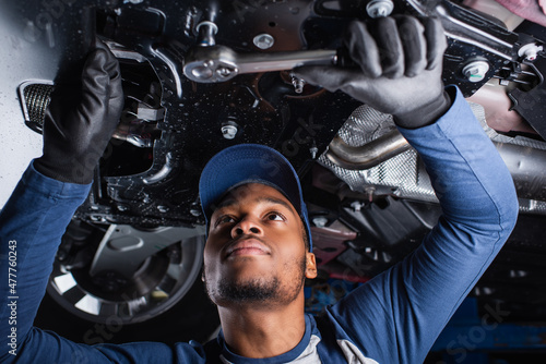 Φωτογραφία Young african american mechanic working with tool under car in garage