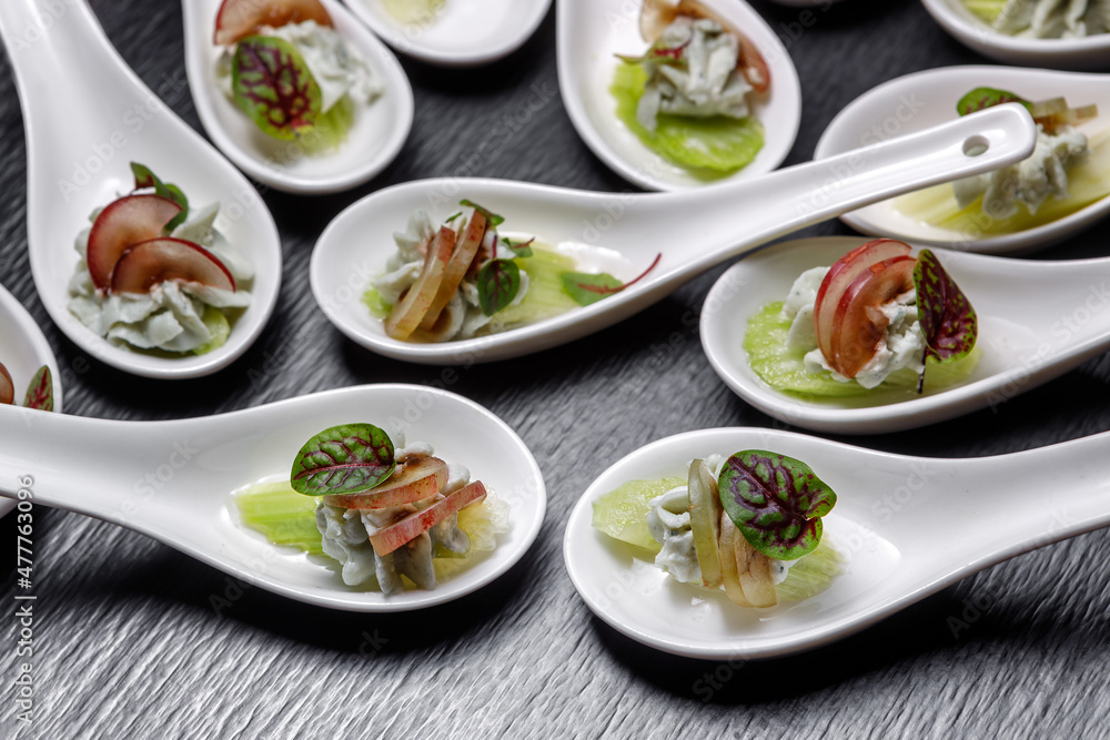 A light meat snack decorated with grapes, celery and leaves, in a dessert spoon is on the table. A light meat snack decorated with grapes, celery and leaves, in a dessert spoon is on the table.