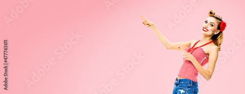 Portrait of amazed happy woman pointing at something. Excited girl in pin up style, showing copy space for text or imaginary. Retro fashion and vintage. Rose pink back.