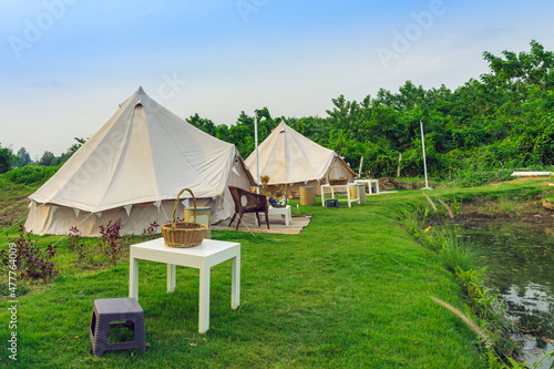 Holiday tents and lounge areas on green lawn place among trees at natural parkland. Camping tent on nature in summer.Travel background. Place for picnic outdoors. Recreation area and camp with tent.